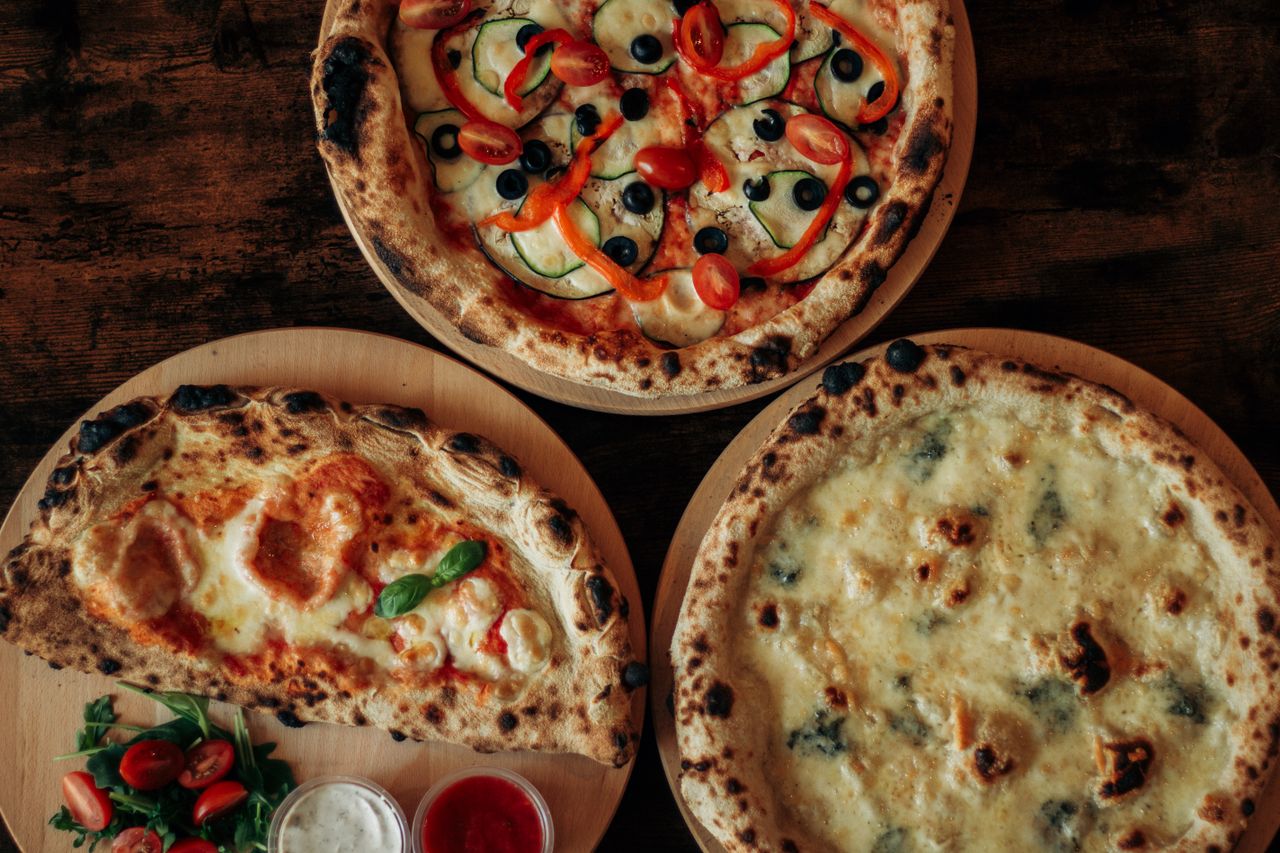 Top view of three assorted pizzas with various toppings on wooden boards.
